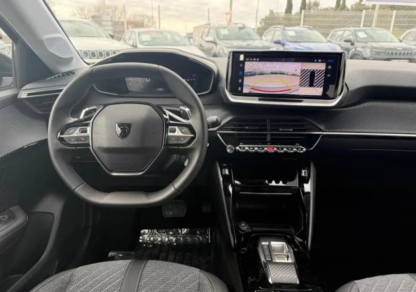 Vue intérieure avant du Peugeot 208 Hybrid 145 Allure 2025, volant compact, écran tactile avec caméra de recul, finition noire et grise.