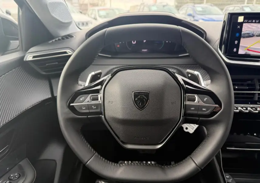 Vue centrée sur le volant noir du Peugeot 208 Hybrid 145 Allure 2025 avec tableau de bord et écran tactile visibles.