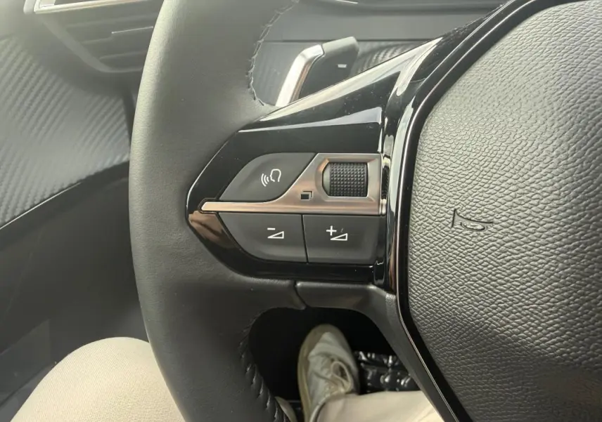 Gros plan sur les commandes du volant noir de la Peugeot 208 Hybrid 145 e-DCS6 Allure, avec détails des boutons multifonctions.