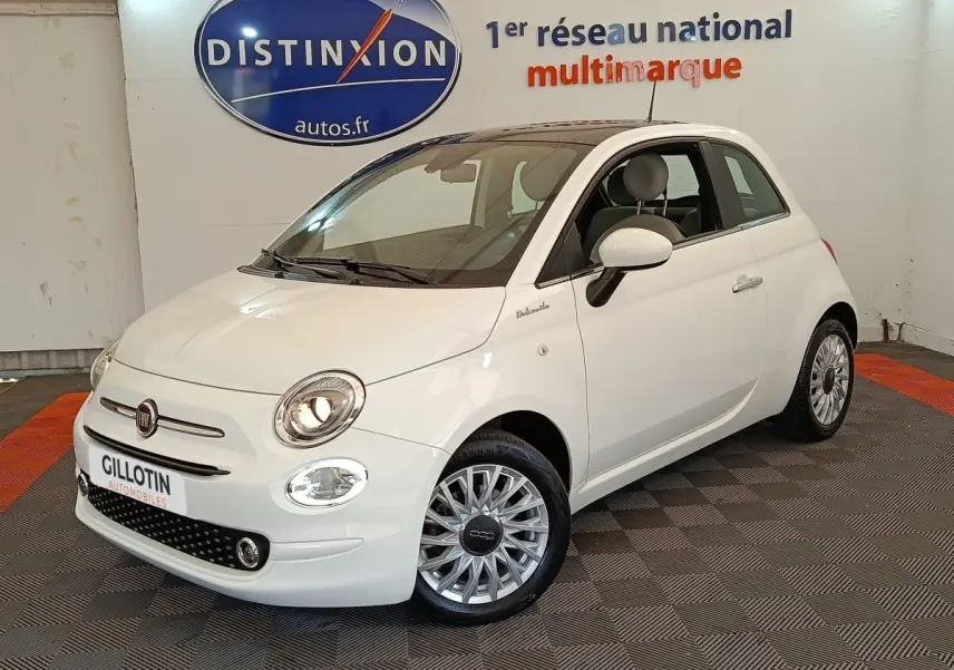 Vue 3/4 avant droite d'une Fiat 500 Dolcevita blanche, avec jantes multibranches et phares allumés en intérieur showroom.