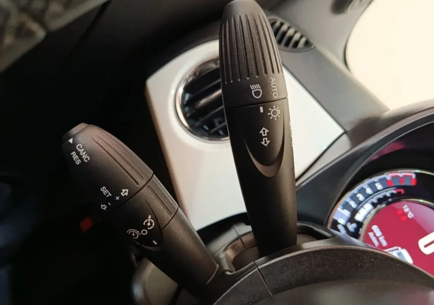 Gros plan sur les commandes de clignotants et régulateur de vitesse du tableau de bord blanc d'une FIAT 500 Hybrid 2022.