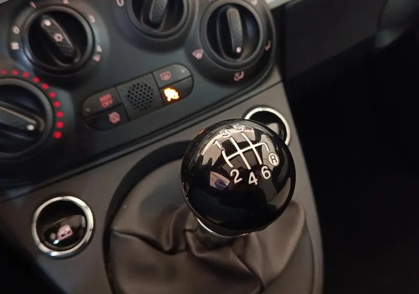 Gros plan sur le levier de vitesses manuel noir de la FIAT 500 Hybrid, avec commandes de climatisation en arrière-plan.