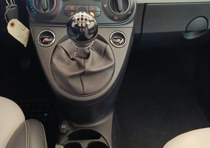 Vue intérieure centrée sur la console centrale et les commandes de climatisation d’une Fiat 500 blanche, version Hybrid.