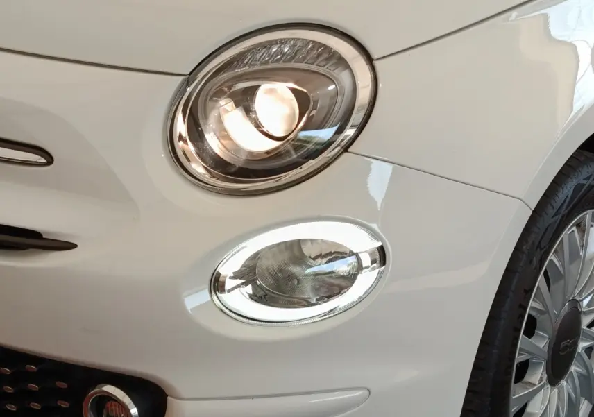 Gros plan sur l'avant droit blanc d'une FIAT 500 Hybrid 2022, mettant en valeur ses phares ellipsoïdaux et la jante distinctive.