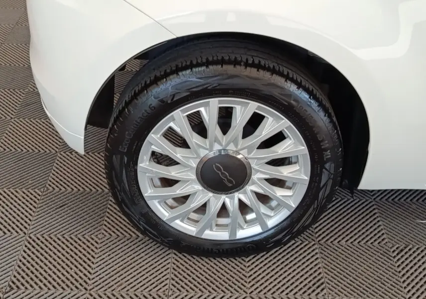 Gros plan sur la roue avant droite d’une FIAT 500 blanche, mettant en valeur la jante argentée au design étoilé.