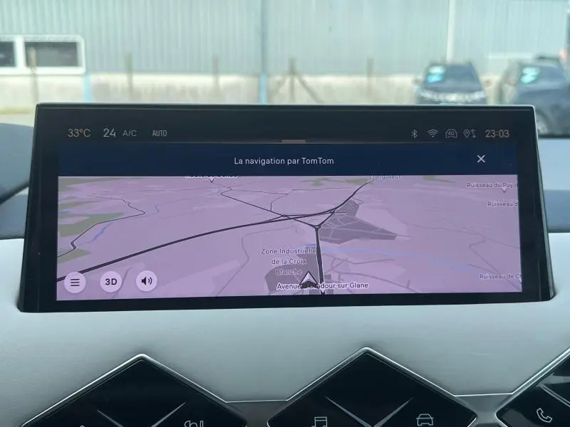 Écran tactile central du tableau de bord du DS3 2024, affichant la navigation TomTom avec vue extérieure floue.