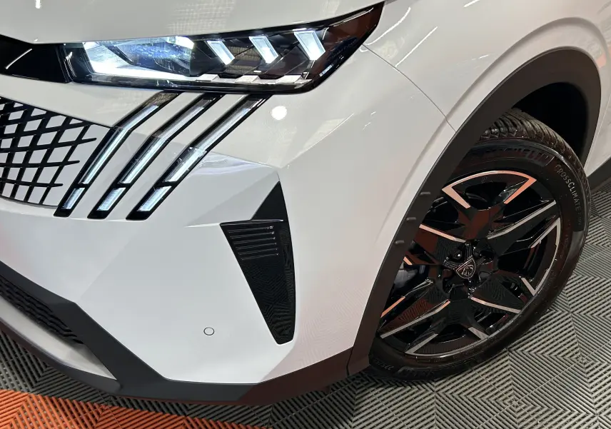 Gros plan sur l’avant droit blanc Okenite du Peugeot 3008 III Hybrid avec phares LED et jante noire biton distinctive.