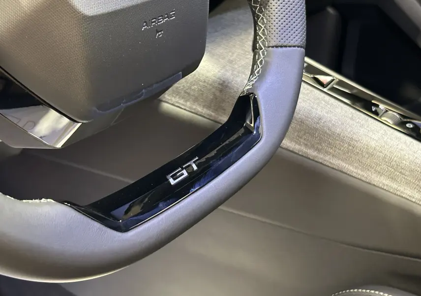 Gros plan sur le volant cuir perforé avec logo GT du Peugeot 3008 III Hybrid, intérieur gris et noir.