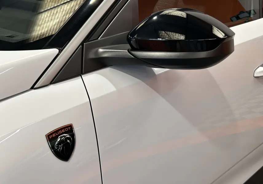 Détail du côté gauche blanc Okenite du Peugeot 3008 III Hybrid avec rétroviseur noir brillant et logo Peugeot sur l'aile.