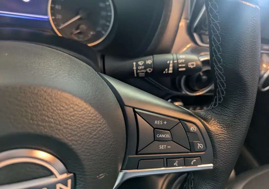 Gros plan sur le volant en cuir noir du Nissan Juke 2024, montrant les commandes de régulateur de vitesse à droite.