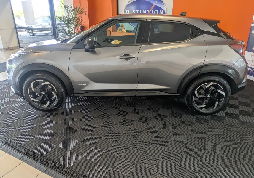 Profil côté gauche du Nissan Juke 2024 gris squale métal, avec jantes noires et toit contrasté en exposition intérieure.