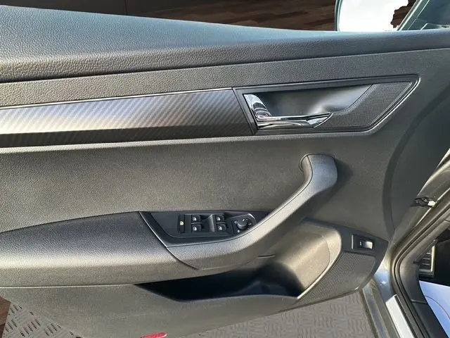 Vue rapprochée de la porte avant gauche du Skoda Karoq gris graphite, avec commandes électriques et insert décor carbone.