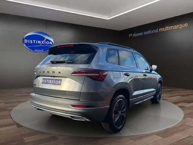 Vue 3/4 arrière droite du Skoda Karoq gris graphite 2025 avec jantes noires et feux arrière LED allumés.