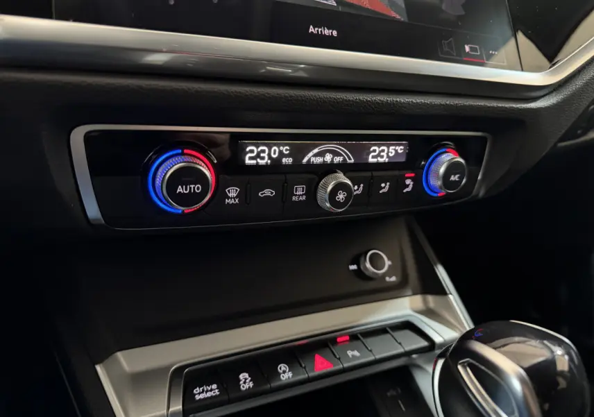 Gros plan sur la console centrale de l'Audi Q3 noire, montrant les commandes de climatisation digitale et la boîte automatique.
