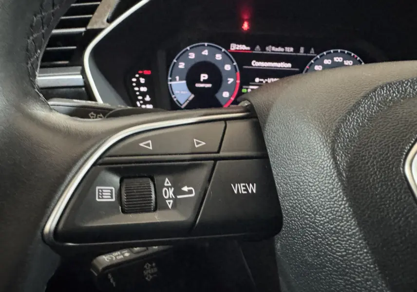 Gros plan sur le volant cuir noir d’un Audi Q3 2022, avec commandes multifonctions et tableau de bord numérique en arrière-plan.