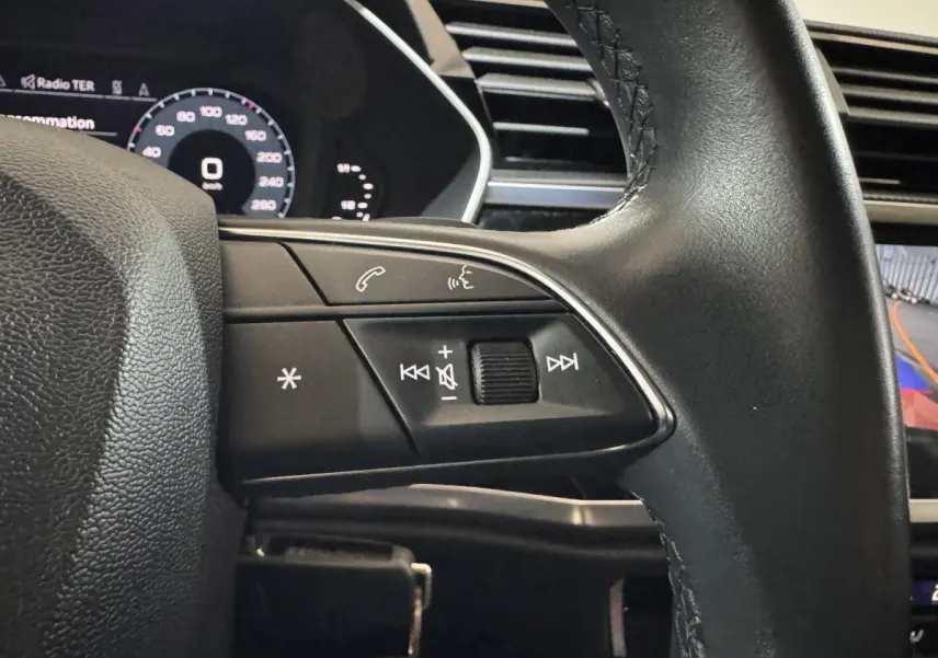 Gros plan sur les commandes au volant côté gauche d’un Audi Q3 noir, avec affichage digital et caméra de recul visible.