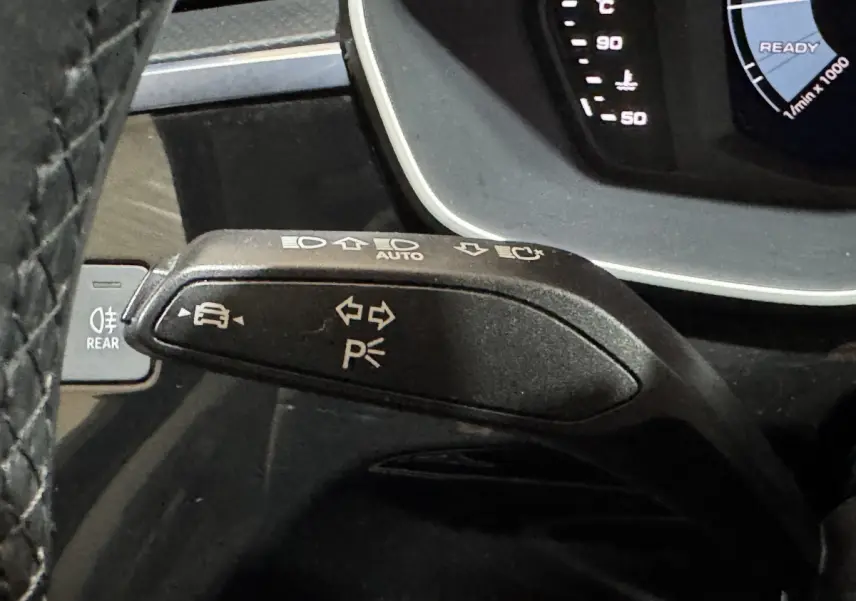 Gros plan sur la manette de clignotants noire avec commandes d'éclairage, tableau de bord numérique partiel d'un Audi Q3 2022.