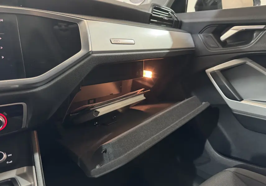 Intérieur Audi Q3 35 TFSI 2022 côté passager, boîte à gants ouverte avec éclairage et tableau de bord noir.