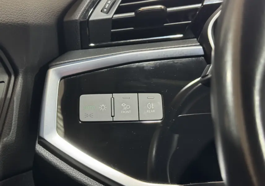 Gros plan sur les commandes d’éclairage à gauche du volant dans l’Audi Q3 noir, finition Business Line 2022.