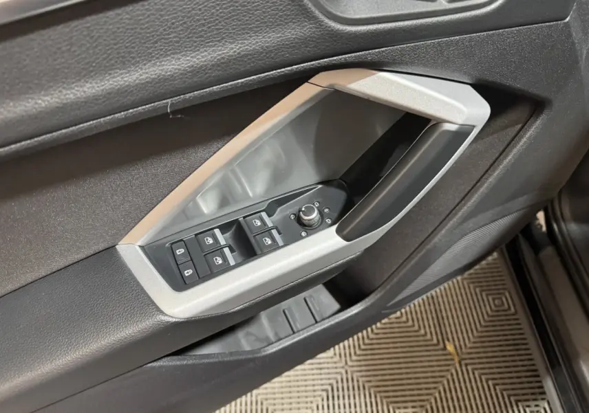 Détail des commandes de lève-vitres et rétroviseurs côté conducteur dans l'habitacle noir de l'Audi Q3 2022.