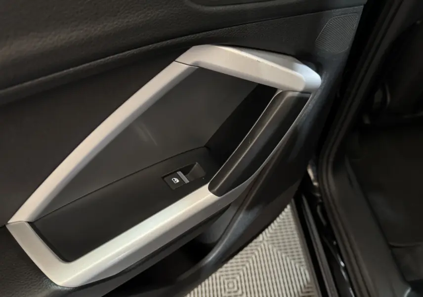 Poignée intérieure côté gauche de porte noire et argentée de l'Audi Q3 35 TFSI 2022 avec bouton de lève-vitre.