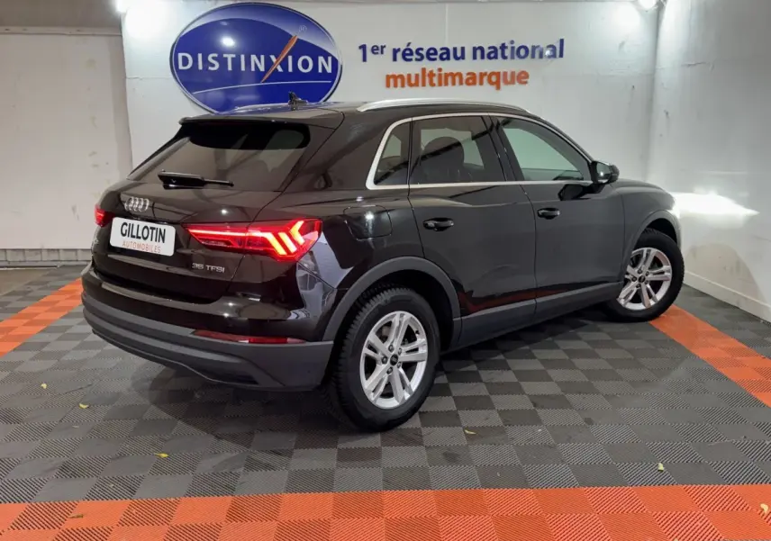 Audi Q3 noir vue 3/4 arrière droit en intérieur, feux arrière allumés et jantes argentées visibles.
