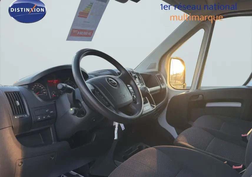 Vue intérieure côté conducteur de l'Opel Movano Fourgon blanc Icy 2023, avec tableau de bord et sièges en tissu noir.