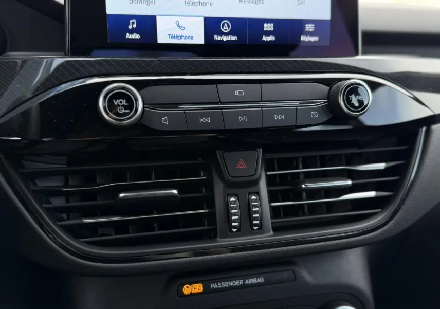 Gros plan sur la console centrale noire du Ford Kuga 2023, avec commandes audio et ventilation visibles.