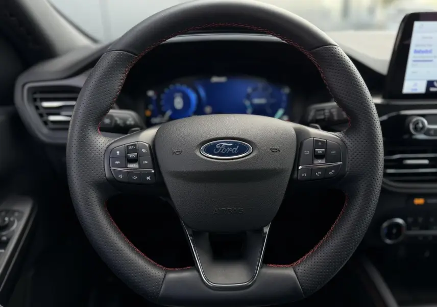 Vue rapprochée du volant noir perforé avec surpiqûres rouges du Ford Kuga 2.0 EcoBlue 120 BVA ST-Line 2023.