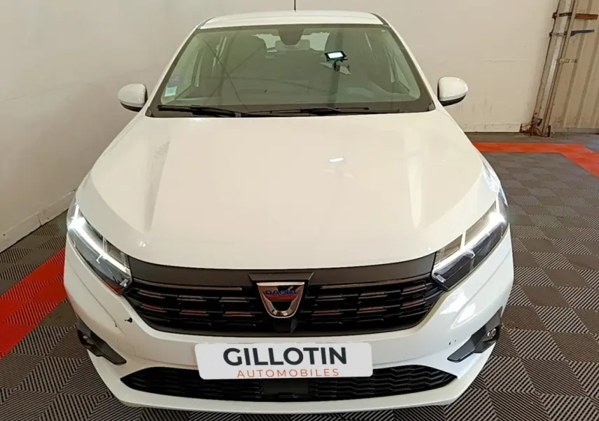 Vue avant d'une Dacia Sandero Confort TCe 90 blanche avec phares LED allumés dans un garage.