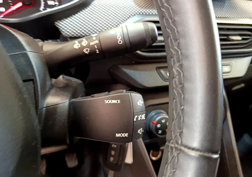 Gros plan intérieur sur le volant noir et la commande multimédia à gauche du tableau de bord de la Dacia Sandero blanche.