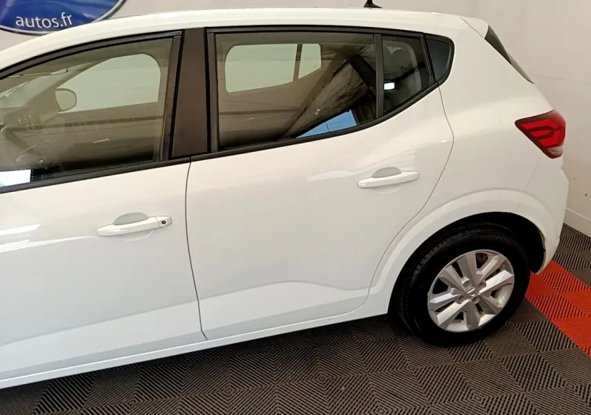 Vue latérale droite d'une Dacia Sandero blanche 2022, mettant en valeur les poignées de porte et la jante alliage.