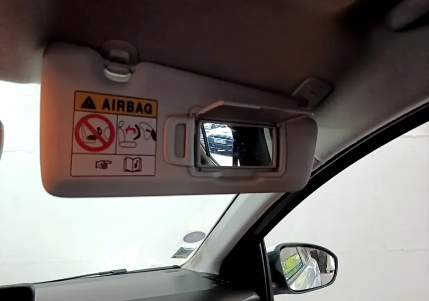Intérieur de la Dacia Sandero blanc, vue sur le pare-soleil conducteur avec miroir et rétroviseur latéral droit.