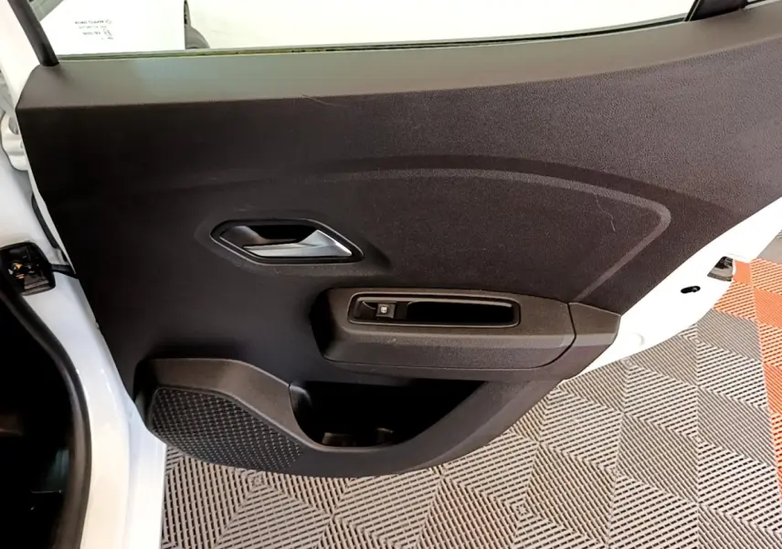 Vue rapprochée de la porte arrière droite noire intérieure d’une Dacia Sandero blanche 2022, avec poignée et commande de vitre.