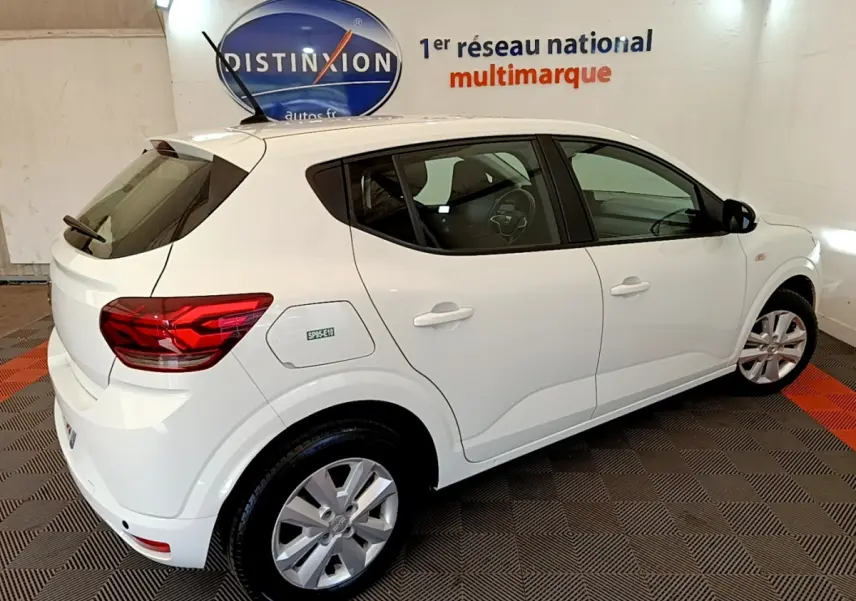 Vue 3/4 arrière droite d'une Dacia Sandero Confort TCe 90 blanche, avec jantes alliage et logo SP95-E10 sur la trappe à carburant.