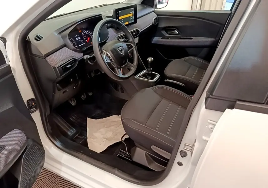 Vue intérieure côté conducteur de la Dacia Sandero blanche 2022, avec tableau de bord moderne et sièges noirs.
