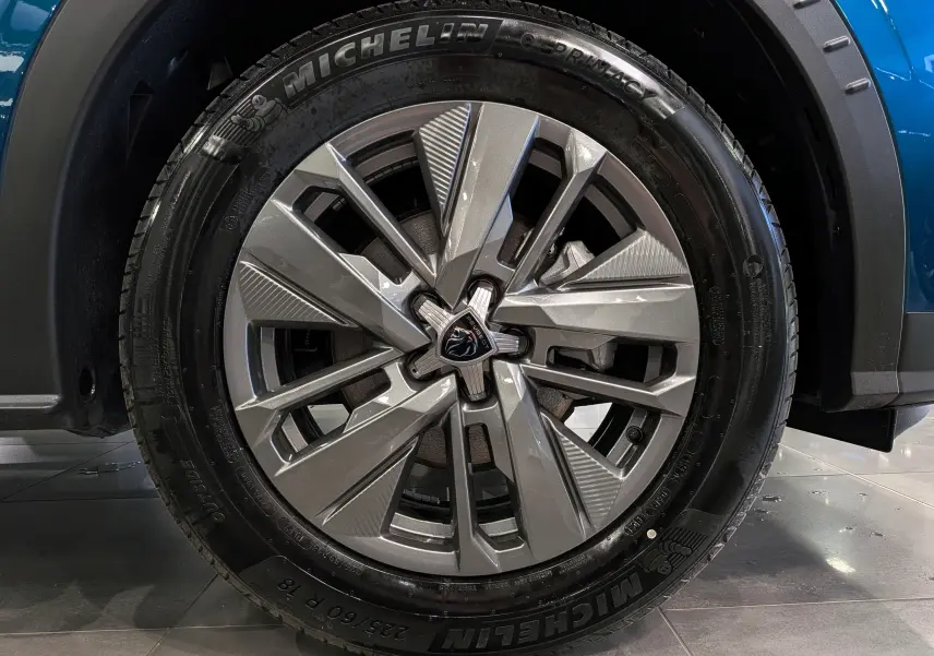 Gros plan sur la roue avant droite d’un Peugeot 3008 Hybrid 145 CH e-DCS6 Allure bleu Obsession avec jante alliage et pneu Michelin.