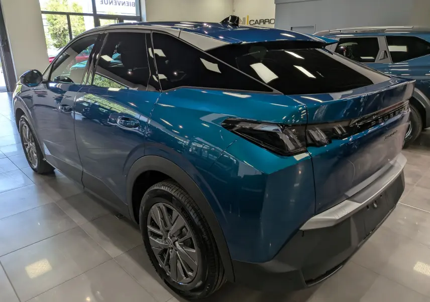 Vue 3/4 arrière droite d’un Peugeot 3008 Hybrid bleu Obsession avec feux arrière noirs et jantes alliage en showroom.