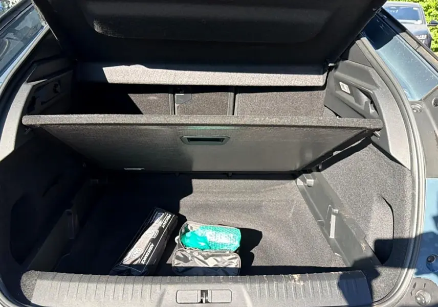 Coffre ouvert vu de l'arrière d'un Peugeot 3008 bleu Ingara, avec plancher mobile et accessoires rangés.
