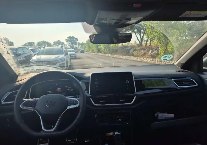Vue intérieure avant du Volkswagen T-Roc 2025 avec tableau de bord noir et écran tactile central.