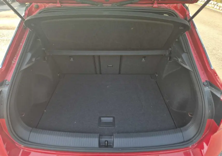 Coffre ouvert vu de l'arrière d'un Volkswagen T-Roc rouge métal foncé, espace de chargement vide et propre.