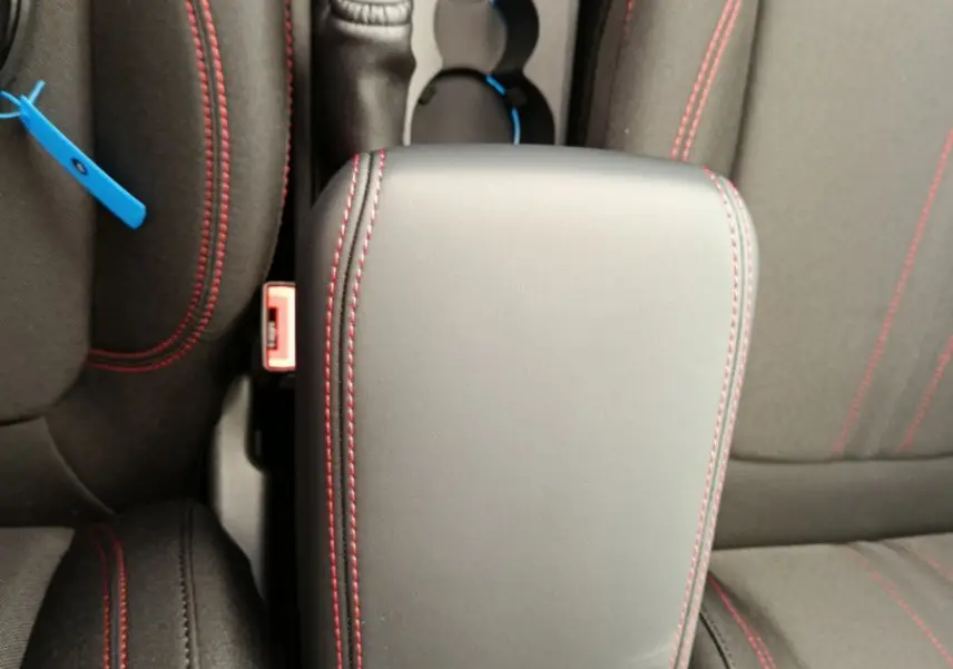 Vue plongeante sur l'accoudoir noir avec surpiqûres rouges entre les sièges avant du Ford Puma ST-LINE 2025.