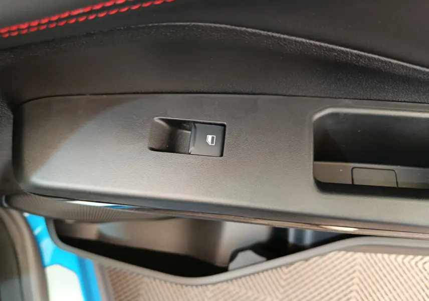 Bouton de commande de lève-vitre sur la porte intérieure noire du Ford Puma bleu, détail côté conducteur.