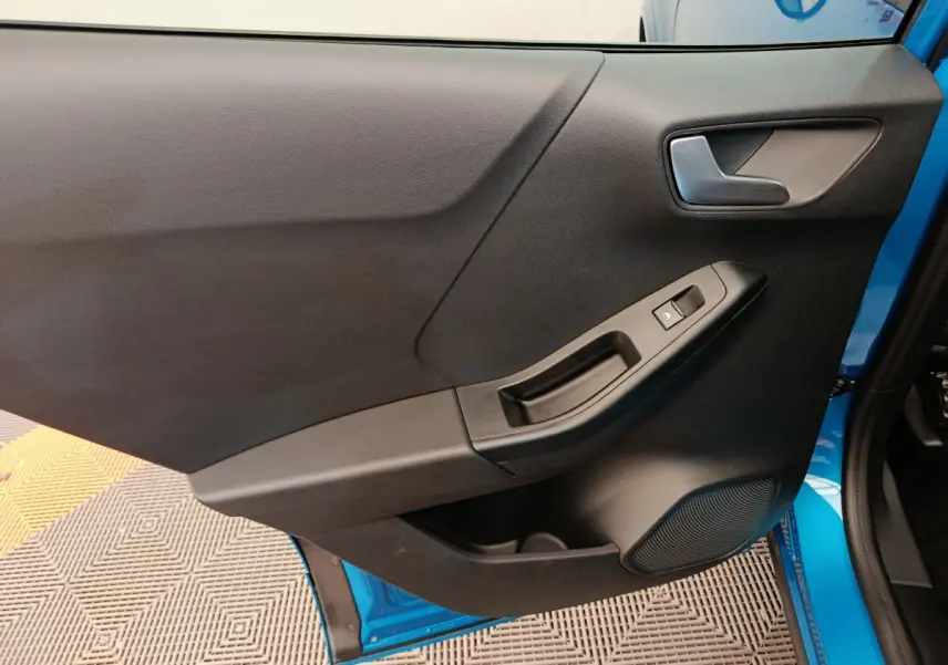 Vue rapprochée de la porte avant gauche noire du Ford Puma bleu 2025, avec poignée et commande de fenêtre électrique.