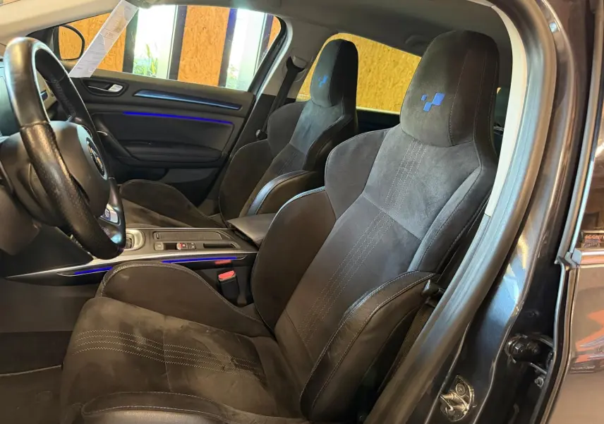 Vue intérieure côté conducteur de la Renault Mégane Break GT 2017, sièges sport noirs avec surpiqûres et logo bleu.