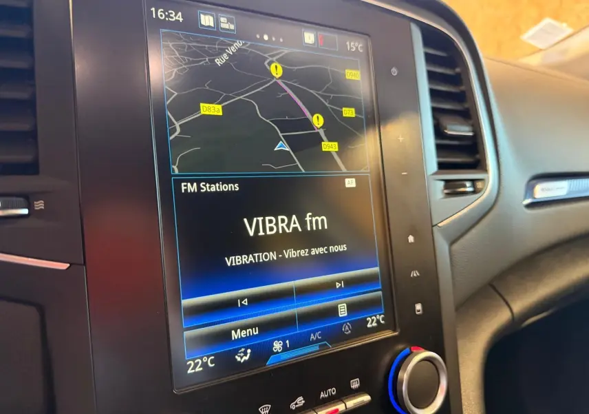 Vue rapprochée de l’écran tactile central du tableau de bord de la Renault Mégane Break GT 2017, affichant la navigation et la radio FM.