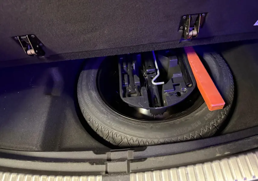 Vue plongeante sur la roue de secours et les outils de la Renault Mégane Break GT 1.6 DCI 165 EDC gris dans le coffre ouvert.