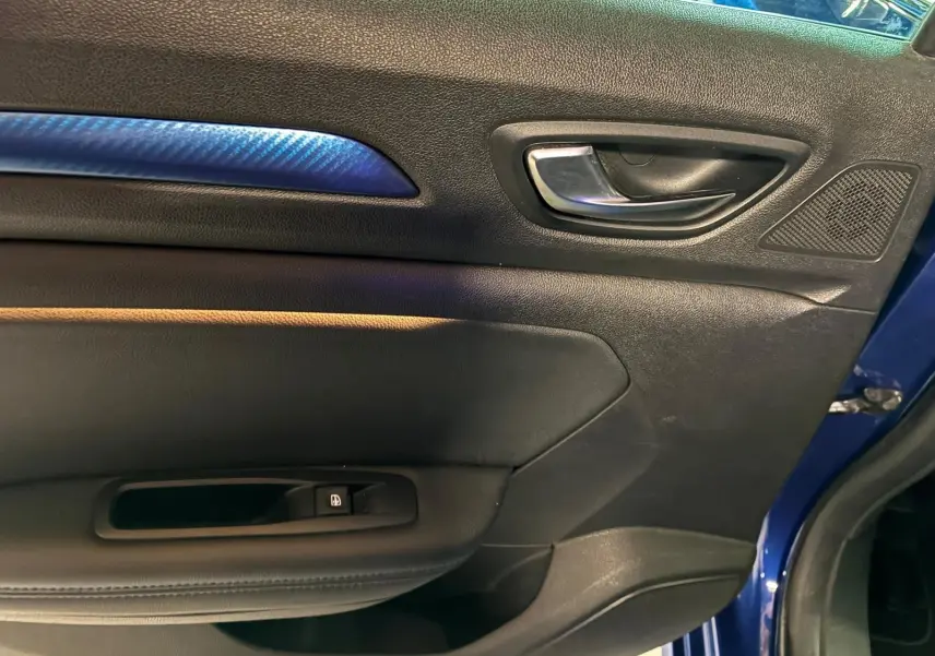 Vue rapprochée de la porte avant gauche d’une Renault Mégane bleu 2019, avec insert décoratif bleu et poignée intérieure chromée.