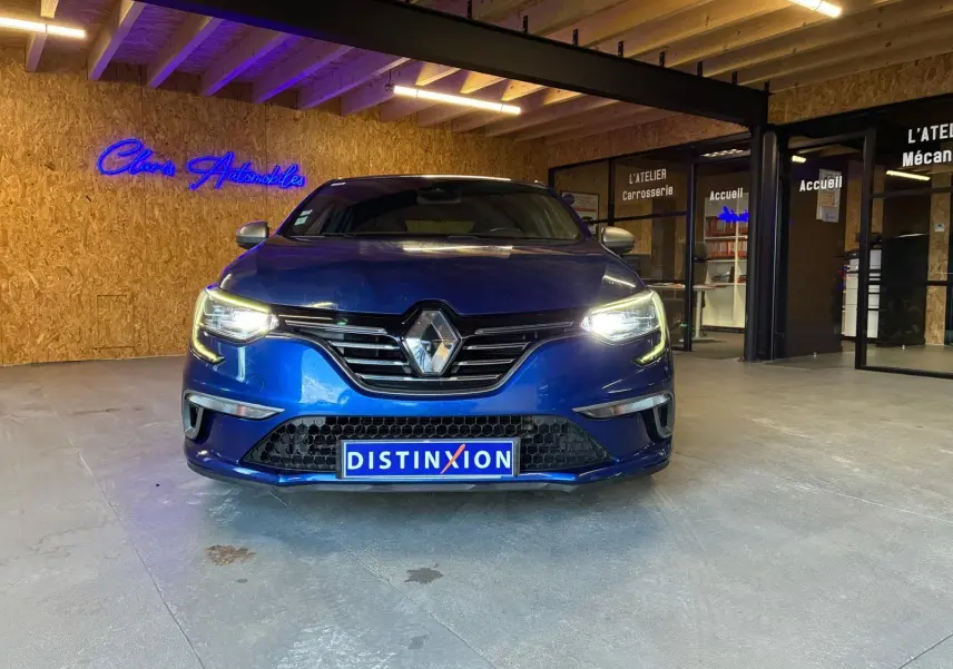 Vue frontale d'une Renault Mégane 1.7 BlueDCI 150 GT Line bleu avec phares allumés dans un showroom.