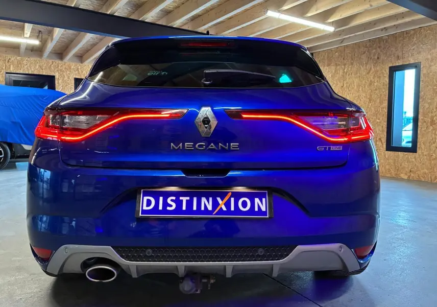 Vue arrière d'une Renault Mégane GT Line bleue 2019 avec feux LED allumés et plaque Distinxion.